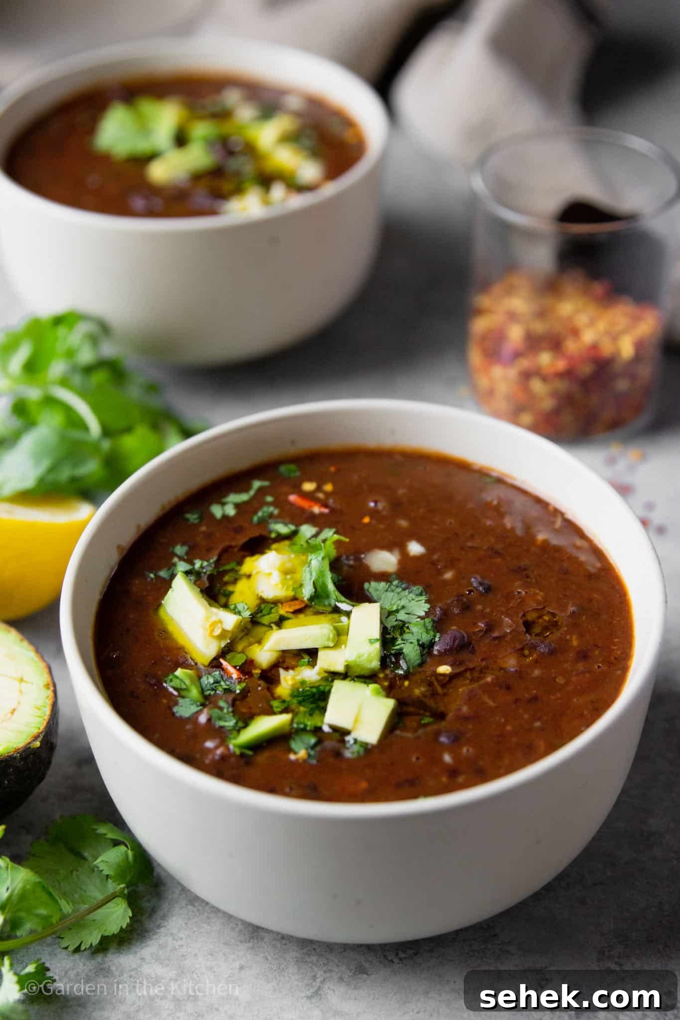 Instant Pot Brazilian Feijoada-Inspired Black Bean Soup 9 close up on black bean soup in a white bowl topped with avocado and cilantro.