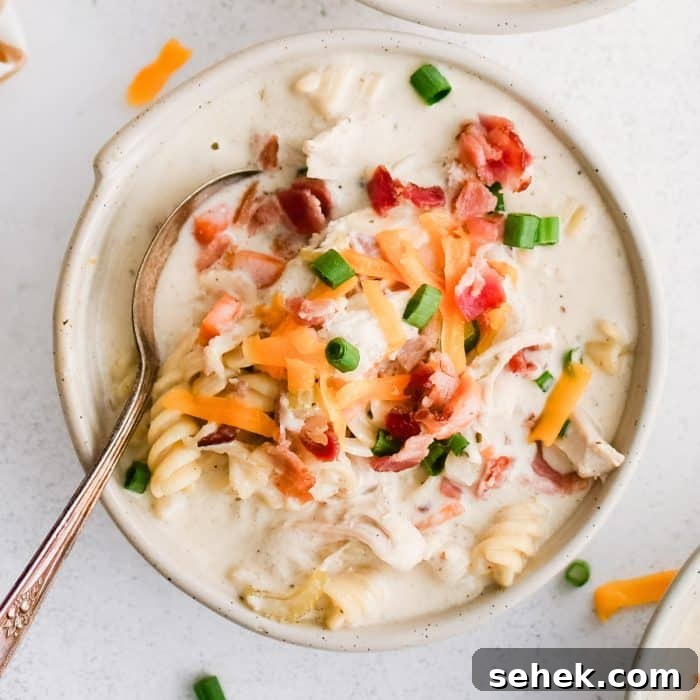 Three white soup bowls filled with super creamy crack chicken soup filled with rotini pasta, shredded chicken, bacon, and topped with shredded cheddar cheese, chopped green onions, and even more crispy cooked bacon bits.
