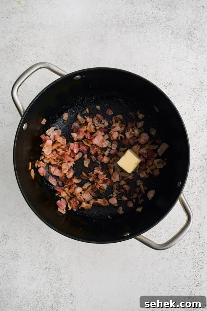 Large soup pot filled with crispy cooked bacon bits and a pat of melting butter.