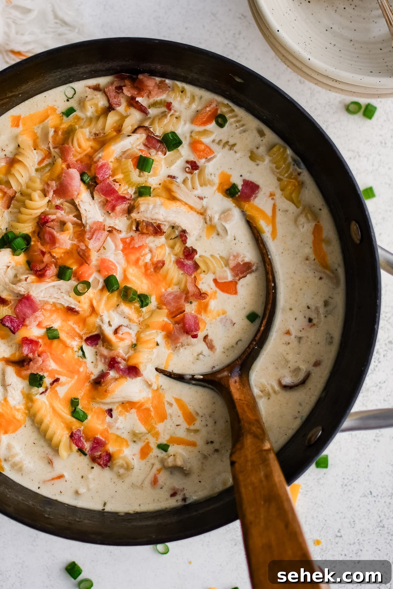 Large soup pot filled with super creamy crack chicken soup made with rotini pasta, shredded chicken, and bacon in a cream based broth, and topped with shredded cheddar cheese, chopped green onions, and even more crispy cooked bacon bits.