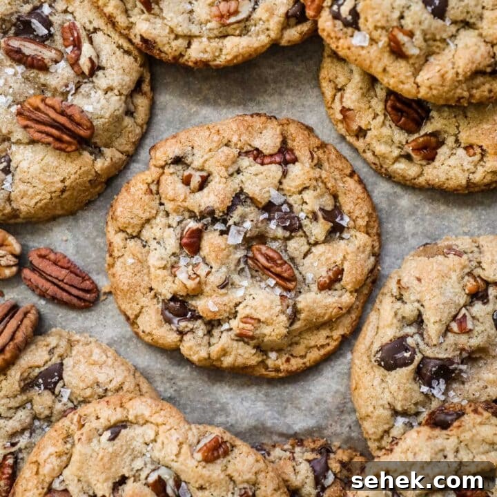 Warm and chewy browned butter pecan chocolate chip cookies with flaky sea salt on a parchment paper-lined baking sheet.