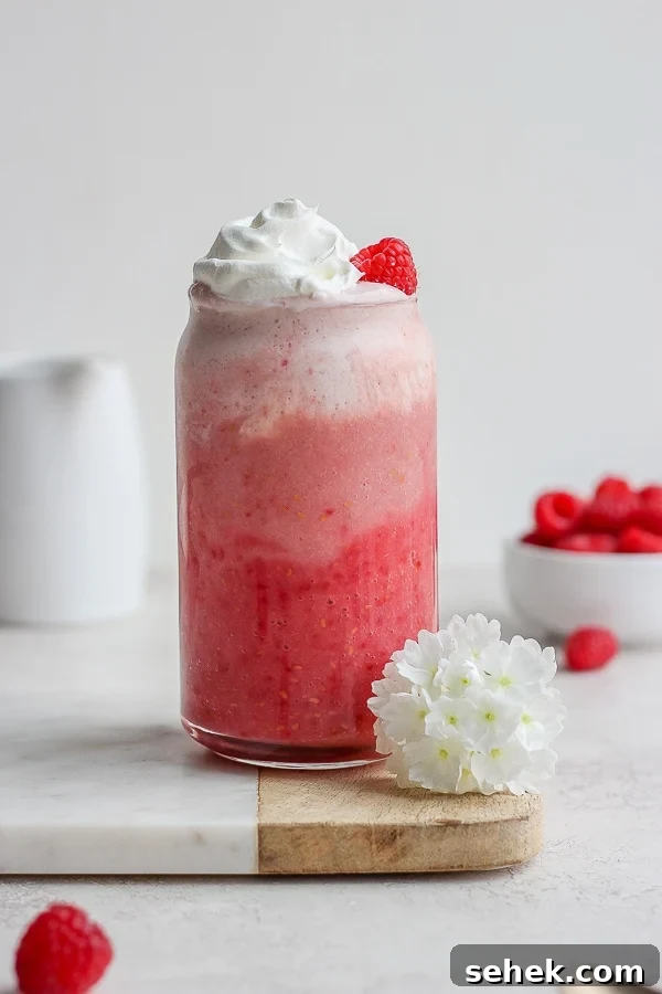 Raspberry Smoothie - a delicious way to use those seasonal raspberries that is simple and healthy! (Dairy-Free!) A raspberry smoothie in a tall glass with whipped cream and a small bowl of raspberries in the background.