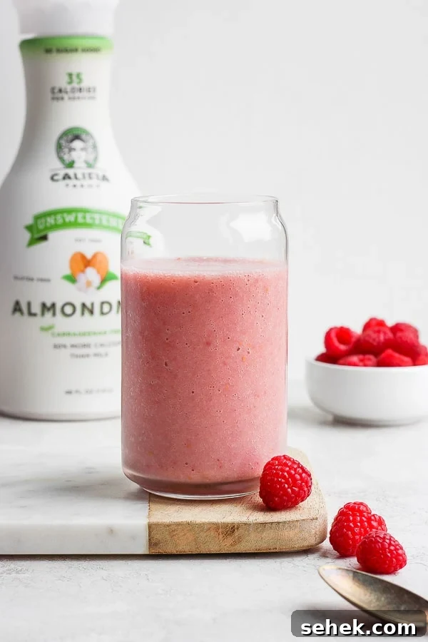 Raspberry Smoothie - a delicious way to use those seasonal raspberries that is simple and healthy! (Dairy-Free!) A raspberry smoothie in a tall glass with fresh raspberries in a bowl and a jug of almond milk in the background.