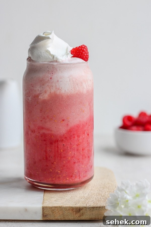Raspberry Smoothie - a delicious way to use those seasonal raspberries that is simple and healthy! (Dairy-Free!) A glass of raspberry smoothie with whipped cream.