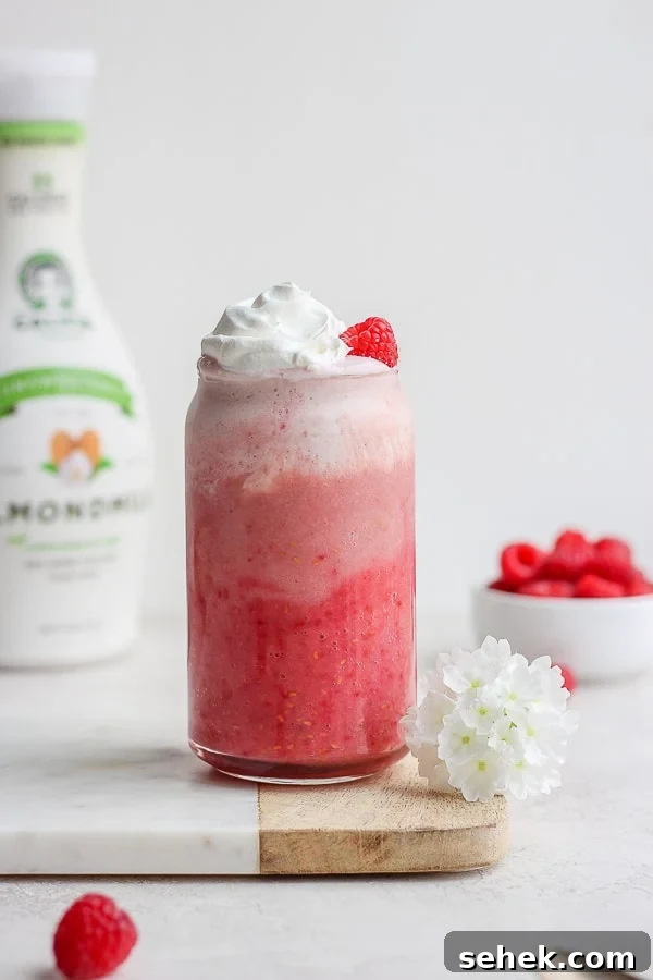 Raspberry Smoothie - a delicious way to use those seasonal raspberries that is simple and healthy! (Dairy-Free!) A raspberry smoothie with a flower next to the glass, raspberries in the background, and a jug of almond milk.