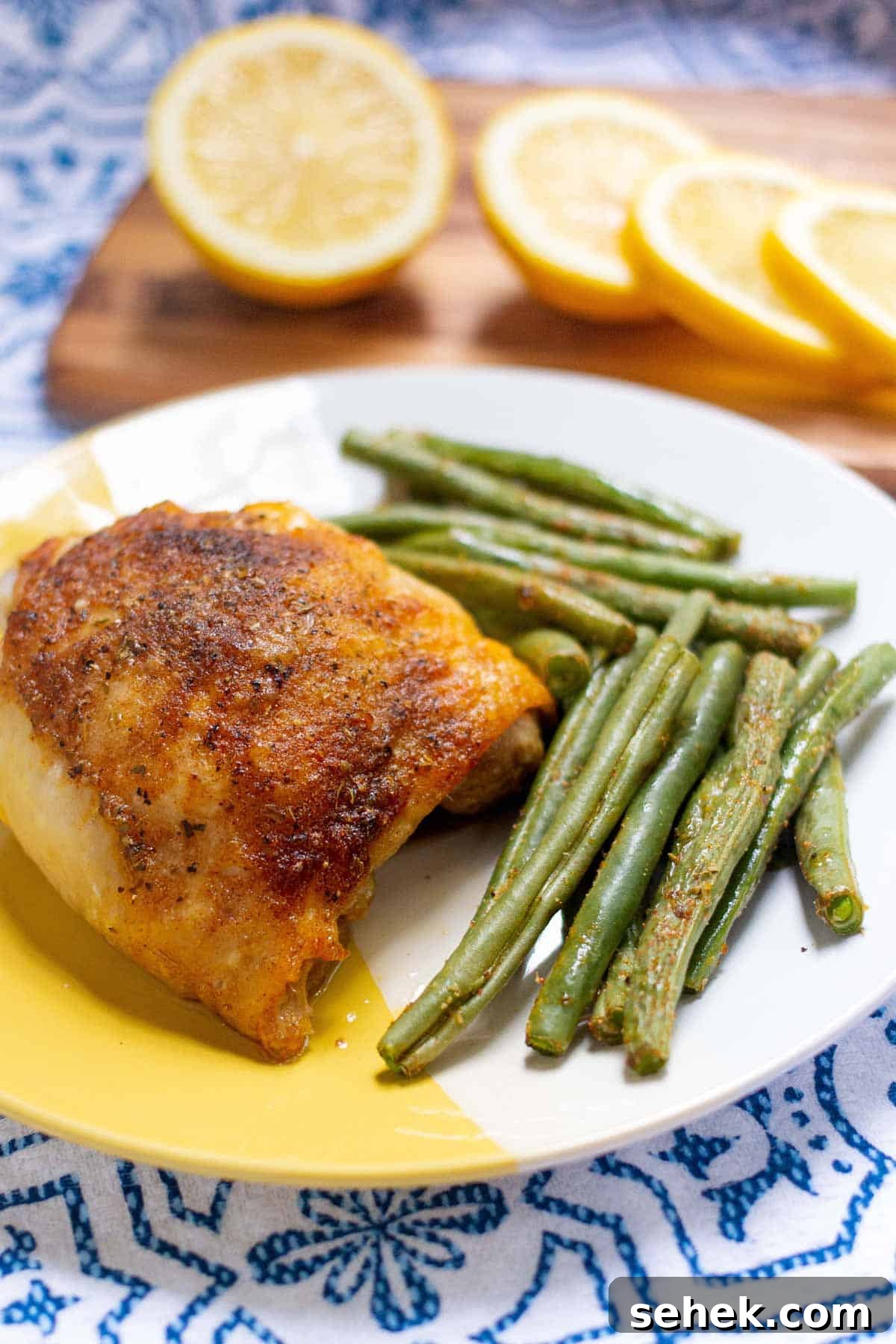 Baked chicken thigh plated with baked green beans.