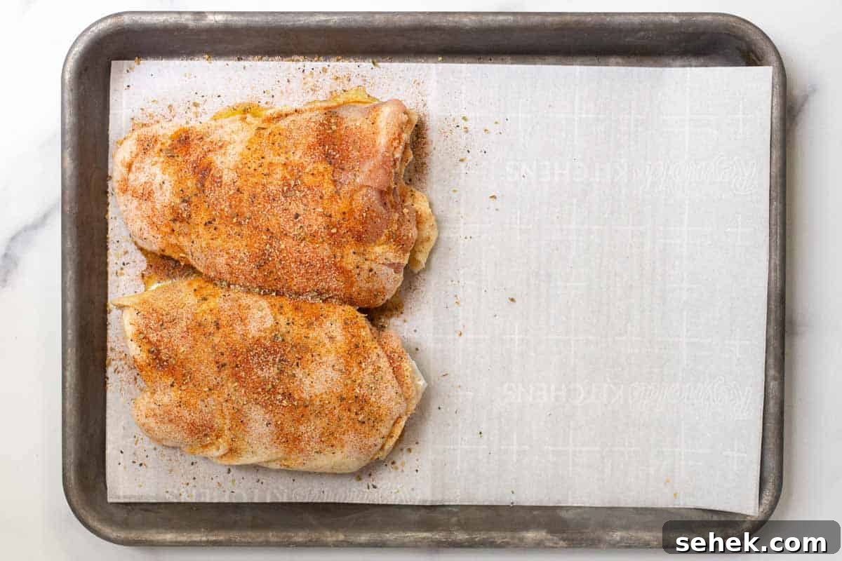 Seasoned raw chicken on one side of the parchment-lined rimmed baking sheet.