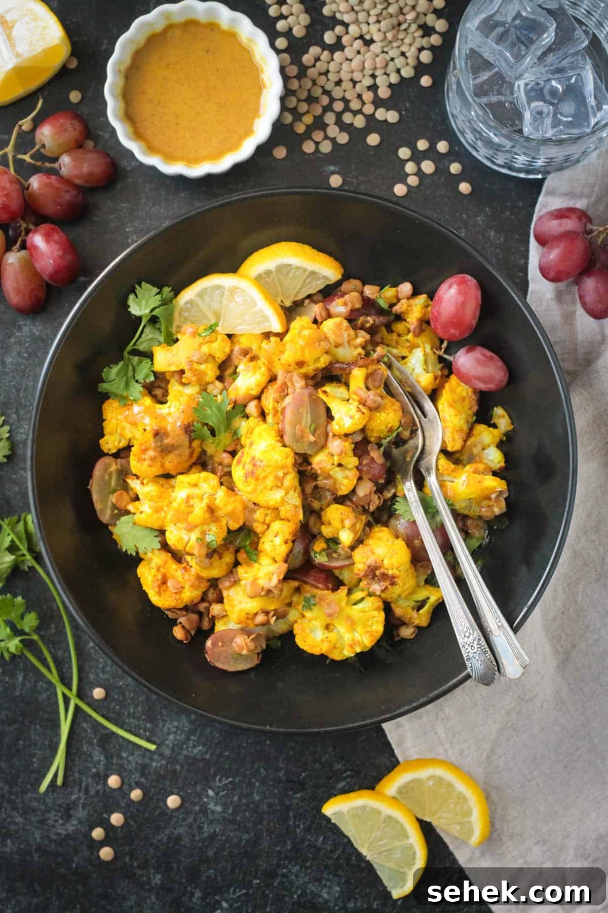 Roasted Cauliflower Salad - cauliflower tossed with turmeric & curry powder, roasted until tender and golden, and then tossed with protein-packed lentils and sweet, juicy grapes. It's flavor and texture dynamite! A light, yet filling, meatless meal or side dish. Two fork in a bowl of curry roasted cauliflower salad with lentils and grapes.