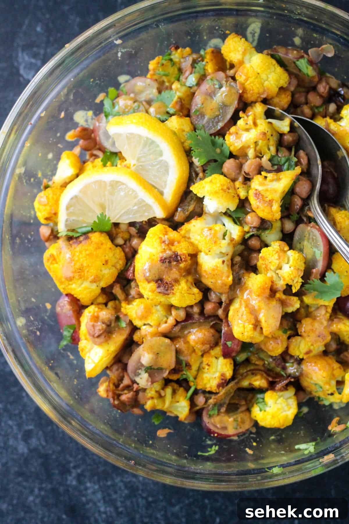 Curry-Roasted Cauliflower Salad with Lemon Tahini Dressing 10 Close up of golden roasted cauliflower, cooked lentils, and sliced grapes in a bowl with curry dressing and lemon wedges.