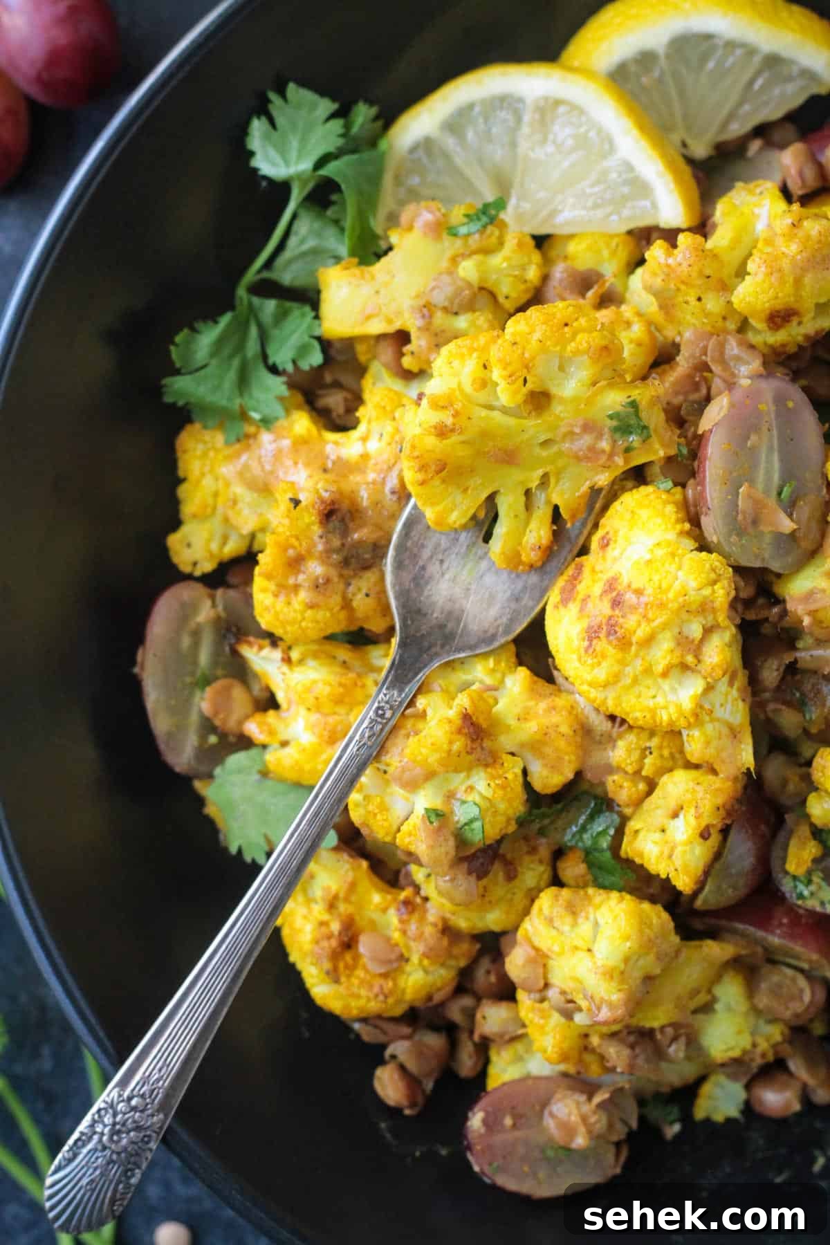 Roasted Cauliflower Salad - cauliflower tossed with turmeric & curry powder, roasted until tender and golden, and then tossed with protein-packed lentils and sweet, juicy grapes. It's flavor and texture dynamite! A light, yet filling, meatless meal or side dish. A fork scooping up a floret of curried cauliflower.