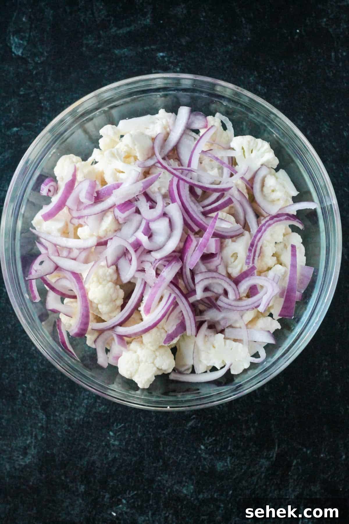Curry-Roasted Cauliflower Salad with Lemon Tahini Dressing 3 Thinly sliced red onion added to the bowl of cauliflower florets.
