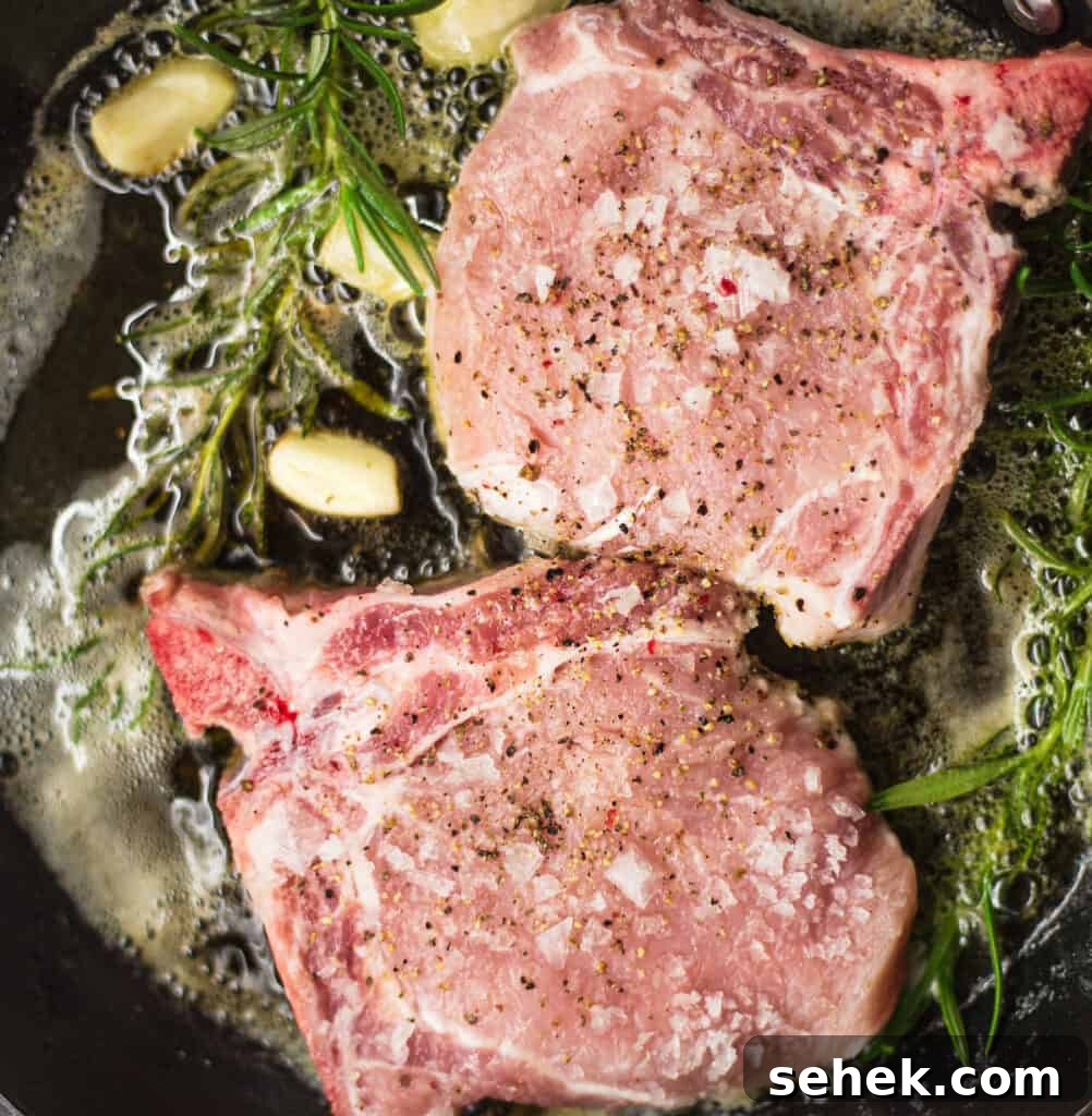 Searing pork chops in a skillet with garlic and rosemary.