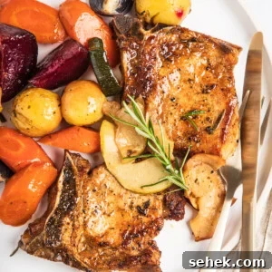 A plate of baked pork chops with apples and winter vegetables, garnished with a sprig of rosemary.