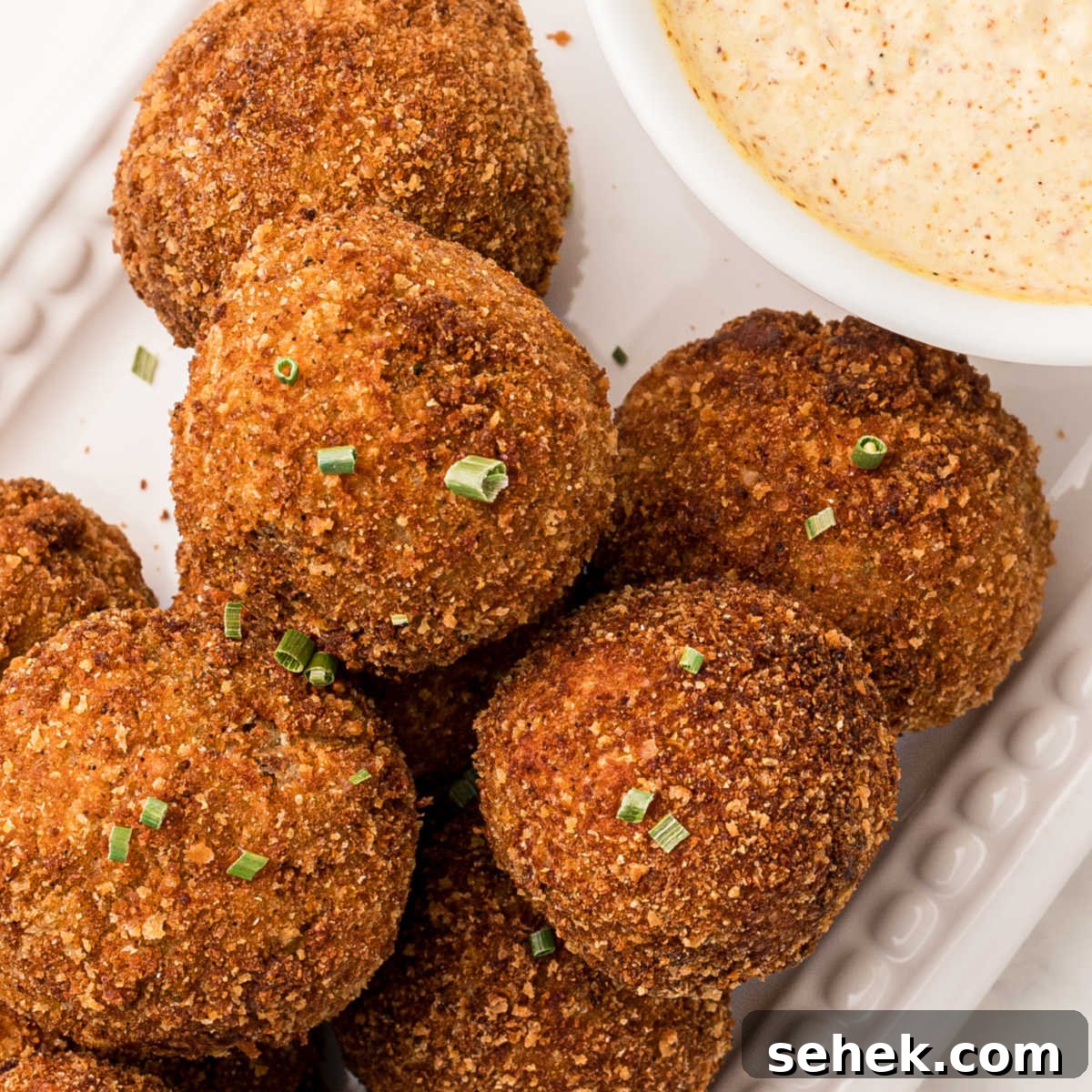 28 Delicious Sides to Serve with Jambalaya 12 Close up of boudin balls with a hint of the mustard cream sauce peeking in, sprinkled with green onions on top.