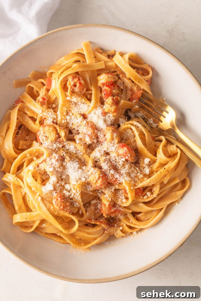 Crawfish Fettuccine topped with Grated Parmesan in a White bowl with a gold fork and spoon.