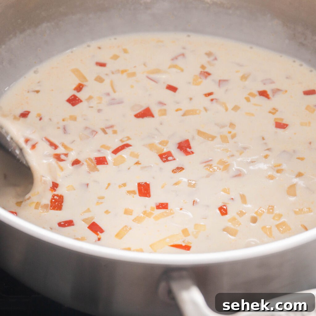 Simmering heavy cream, half and half, diced onions, red bell pepper, and mince garlic in a stainless steel sauce pan.