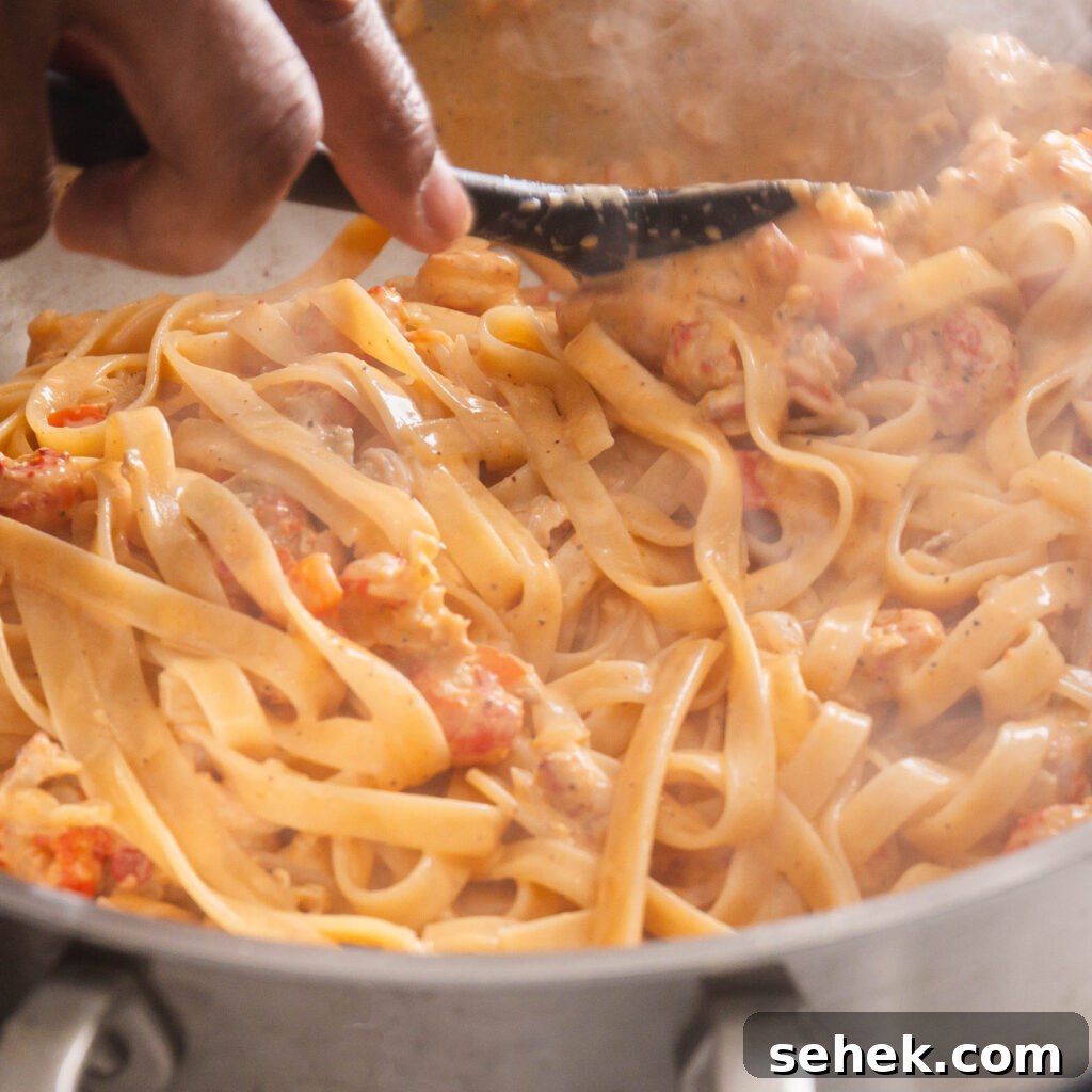 Stirring cooked pasta into the Crawfish Alfredo sauce.