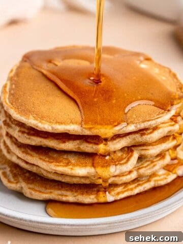 Pouring maple syrup on top of a stack of fluffy cinnamon honey pancakes.