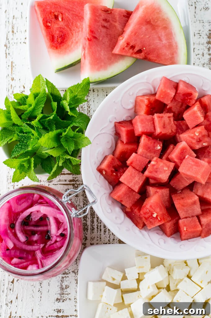 Watermelon Arugula Salad with Feta & Mint 3 A white bowl of cubed watermelon, 3 sliced watermelon pieces, fresh mint and a jar of pickled onions. Cubed feta cheese is on a small white platter.