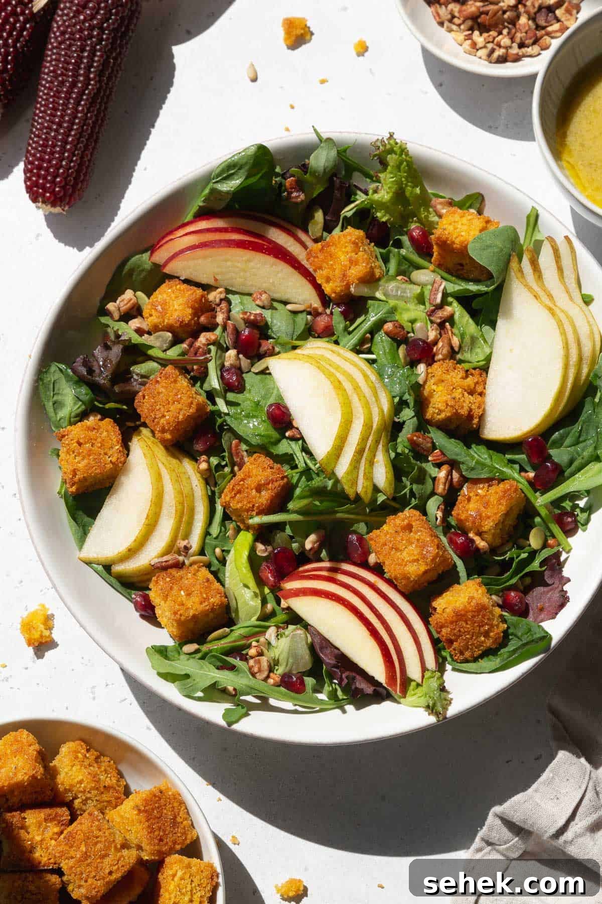 Crispy Cornbread Croutons for Salads and Soups 15 An overhead shot of a large white bowl of salad with cornbread croutons, sliced pears and apples, and pomegranate seeds.