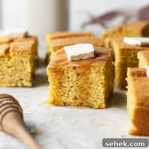 A piece of gluten-free cornbread with a pad of butter and drizzle of honey.