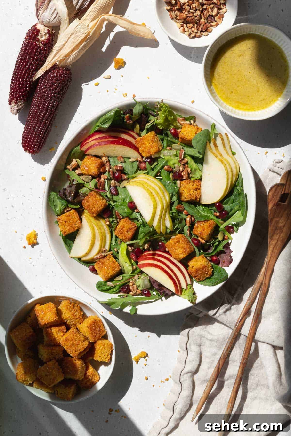 Crispy Cornbread Croutons for Salads and Soups 5 A spread of salad with cornbread croutons, pears, apples, dressing, and salad tongs.