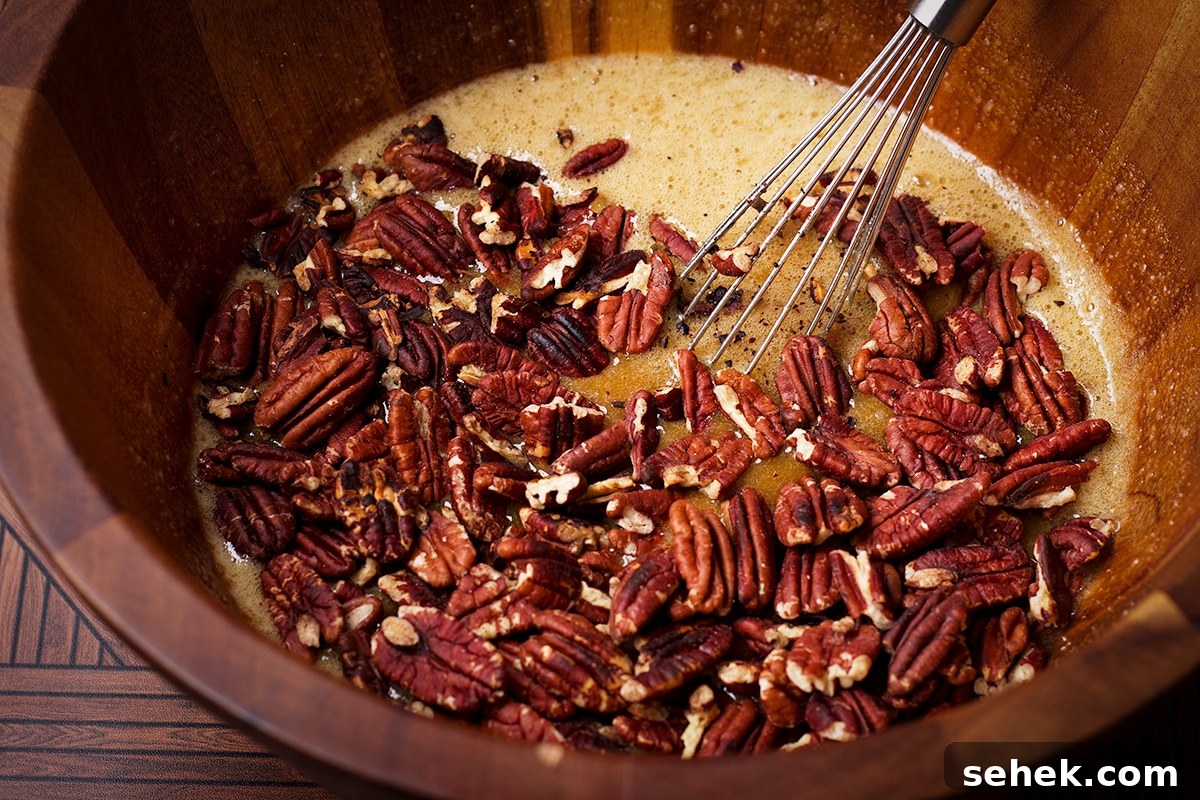 Someone using a wire whisk to stir toasted pecans into the other ingredients for pecan pie filling.