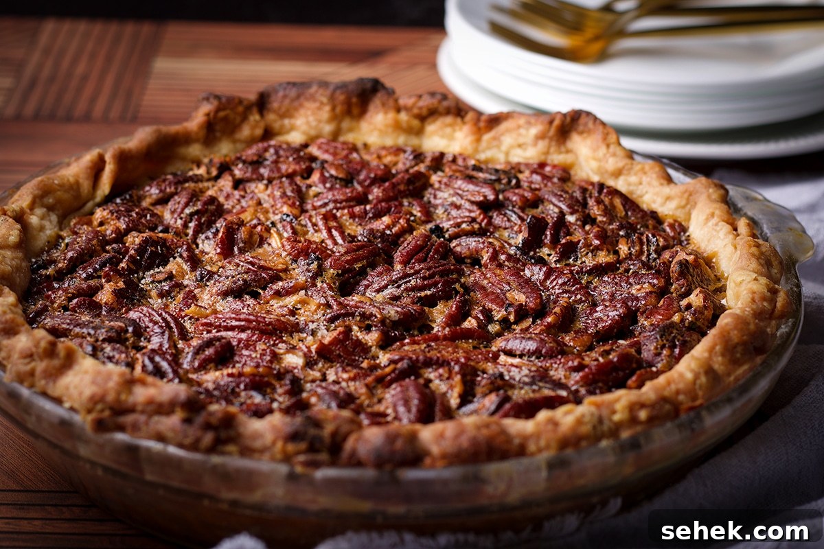 A warm, freshly baked homemade pecan pie resting on a wood table with a stack of plates and forks behind it.