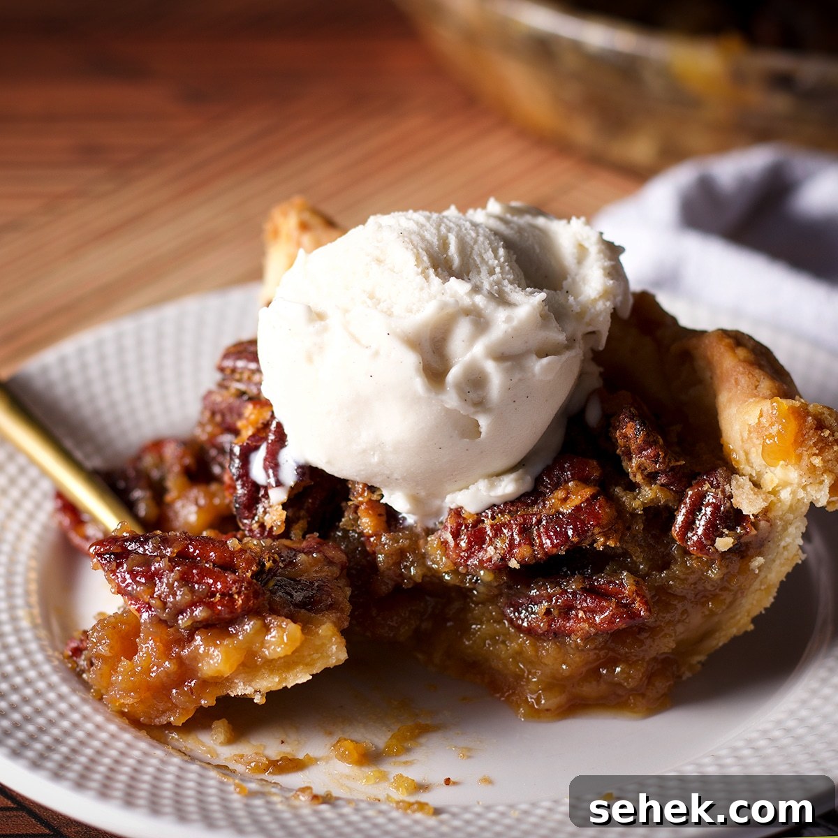 Someone using a gold fork to cut a bite of pecan pie from a slice.