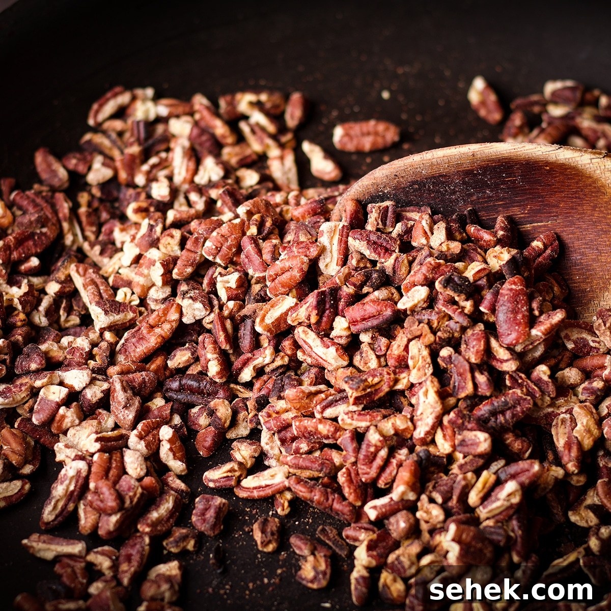 Someone using a wood spoon to stir chopped pecans in a skillet while they toast.