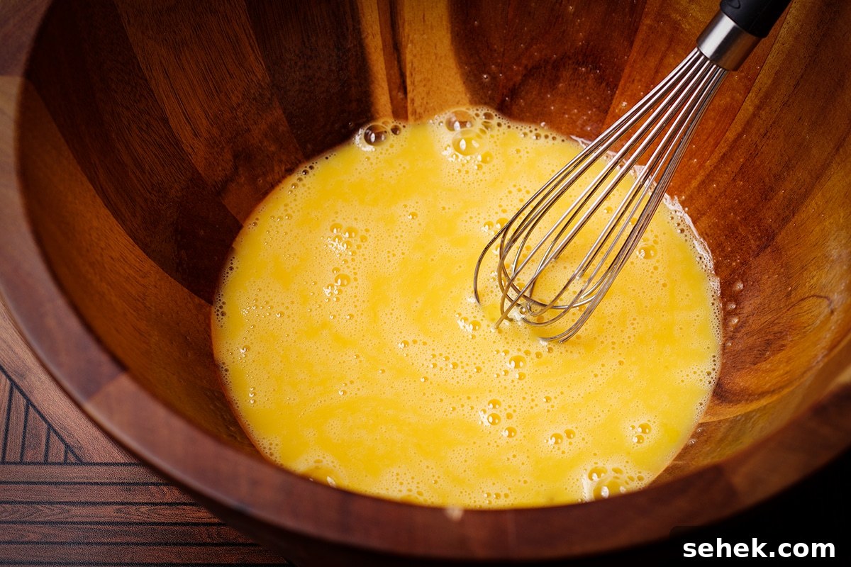Someone using a wire whisk to beat egg yolks in a wood bowl.