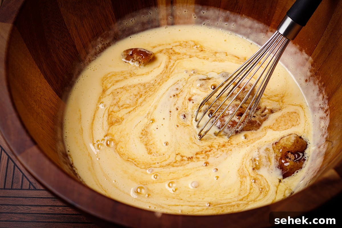 Someone using a wire whisk to mix brown sugar into beaten egg yolks.