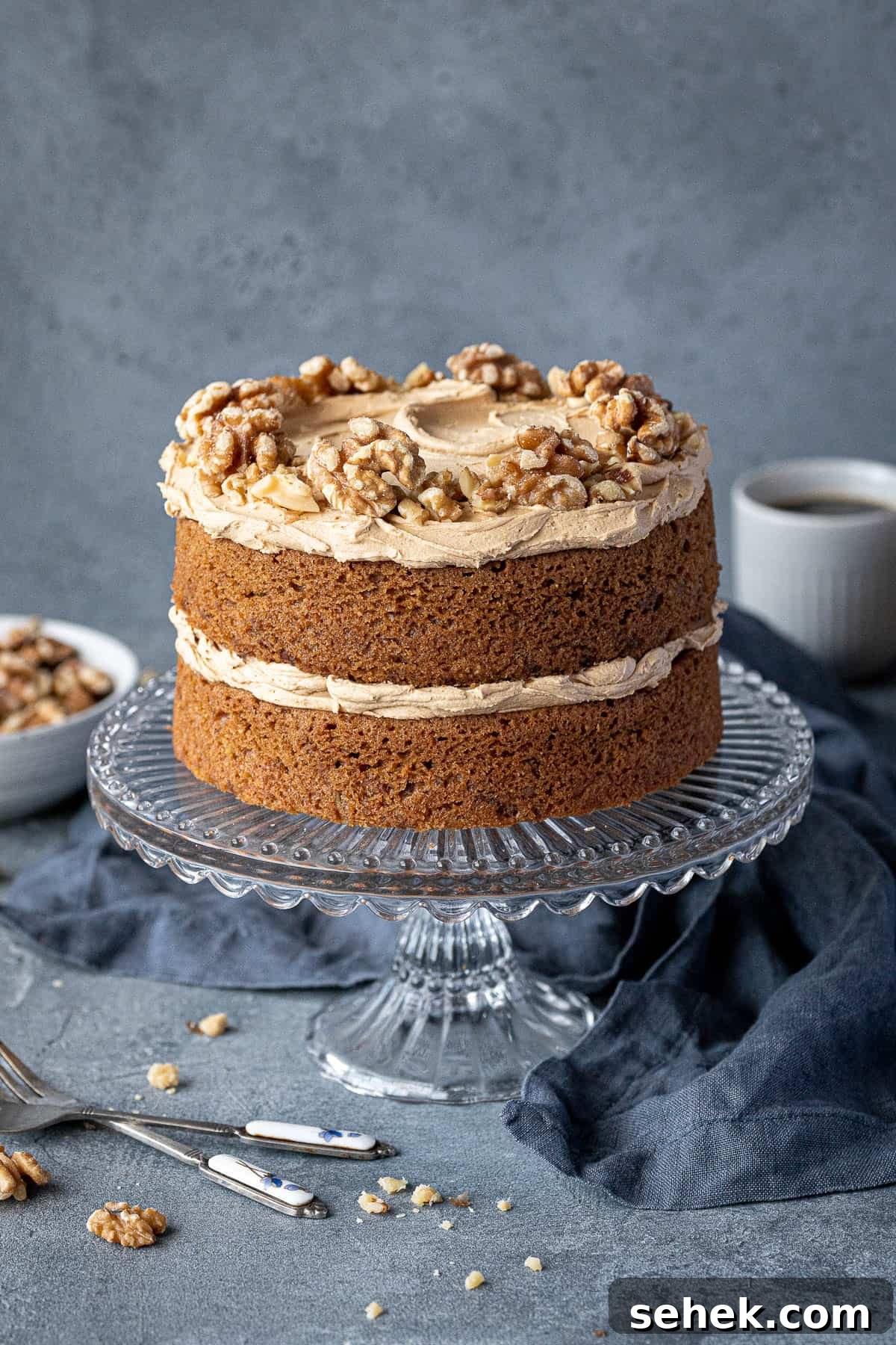 Vegan Gluten-Free Coffee and Walnut Cake Recipe 2 Gluten-free vegan coffee and walnut cake on a glass cake stand with a bowl of walnuts and cups of coffee.