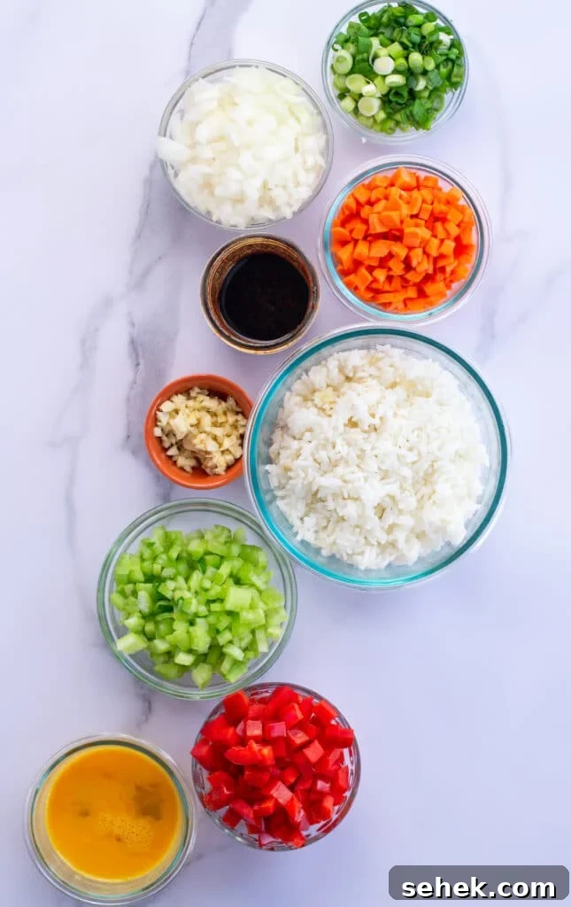 15-Minute Gochujang Fried Rice Recipe 3 Bowls of each ingredient for fried rice including green onions, sweet onion, carrots, soy sauce, leftover white rice, garlic, celery, bell pepper, eggs