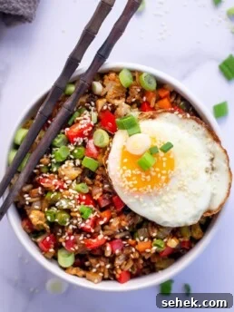 Bowl of gochujang fried rice topped with a fried egg, sesame seeds and green onions