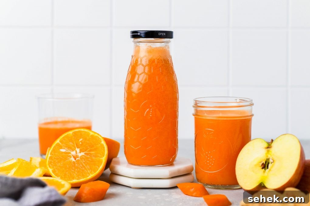 Carrot, Apple and Orange Juice with Ginger 3 Straight on shot of a textured glass jar filled to the brim with bright orange carrot, apple, and orange juice with ginger. Next to some cut oranges, carrot pieces, and other glass jars of juice - on a light colored background.
