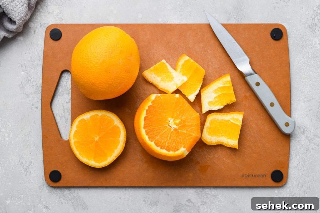 Carrot, Apple and Orange Juice with Ginger 5 Image of a cutting board with 2 oranges. One is whole and the other is cut open, and the peel is being cut away with a small paring knife.