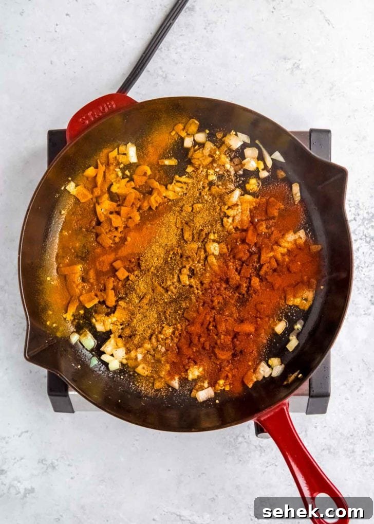 Creamy Indian Butter Chicken Recipe 7 spices being added to skillet with onion, ginger, and garlic