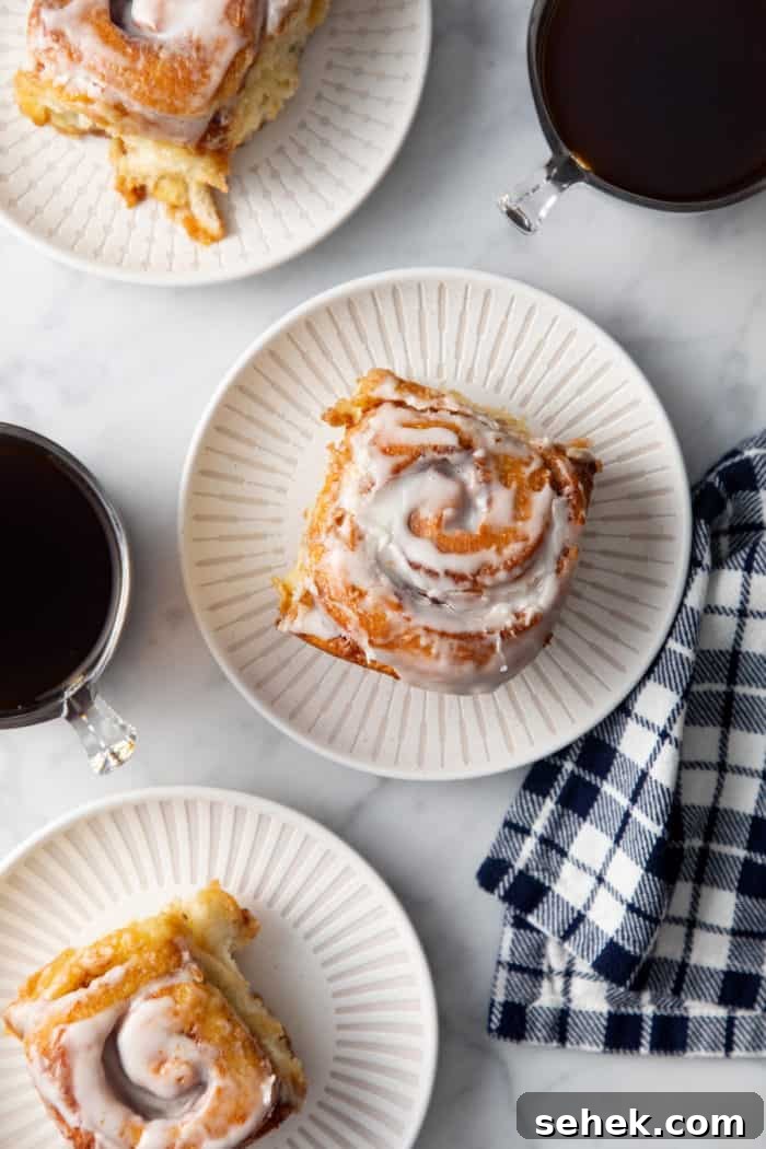 TikTok Cinnamon Rolls Made with Heavy Cream 2 Overhead view of 3 white plates, each with a frosted cinnamon roll on it.