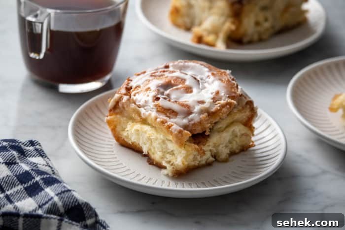 TikTok Cinnamon Rolls Made with Heavy Cream 9 White plate holding a tiktok cinnamon roll. A cup of coffee and a second cinnamon roll are in the background.