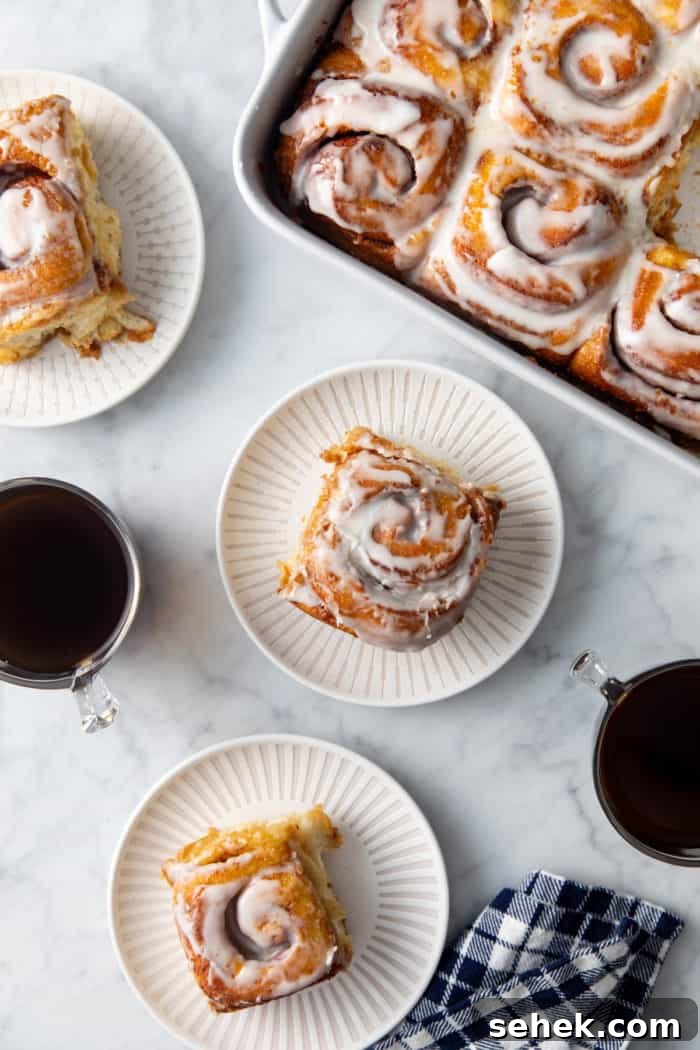 TikTok Cinnamon Rolls Made with Heavy Cream 10 Three white plates with tiktok cinnamon rolls set on a marble countertop next to a baking dish of cinnamon rolls.