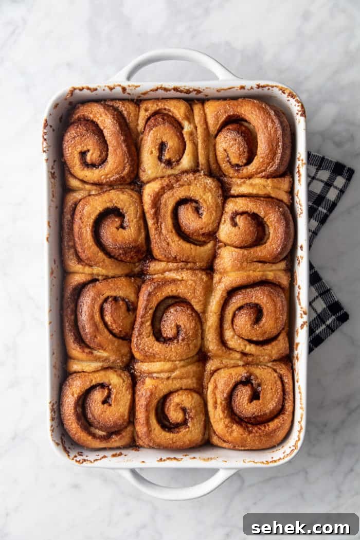TikTok Cinnamon Rolls Made with Heavy Cream 7 Baked cinnamon rolls with heavy cream in a white baking dish, set on a tea towel to cool.