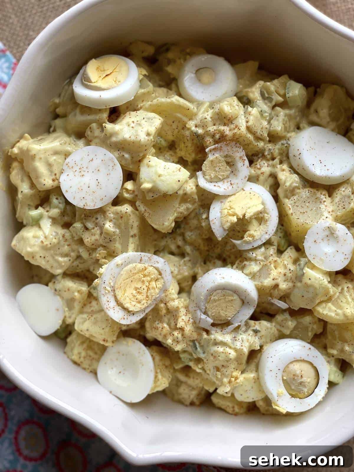 Classic Southern Potato Salad Recipe 6 A white serving bowl of southern potato salad with yellow mustard, topped with hardboiled eggs.