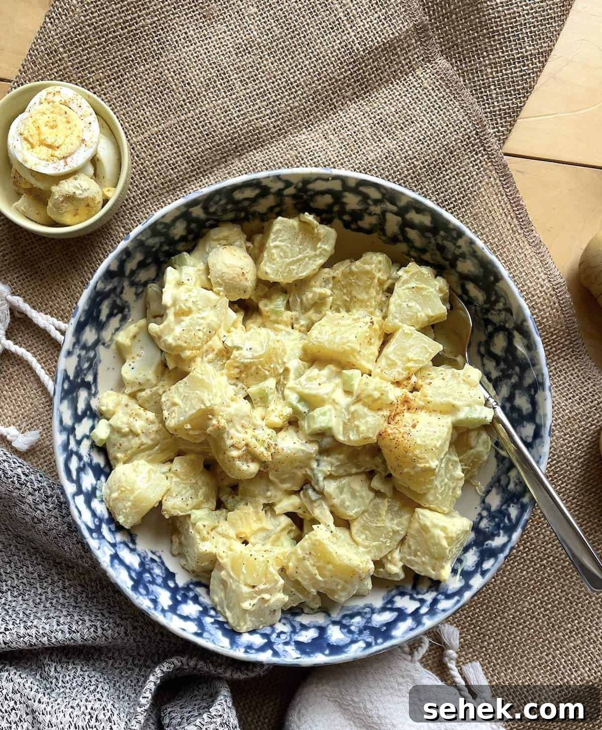 Classic Southern Potato Salad Recipe 8 A bowl of southern potato salad with mustard dressing and hard-boiled eggs on the side.