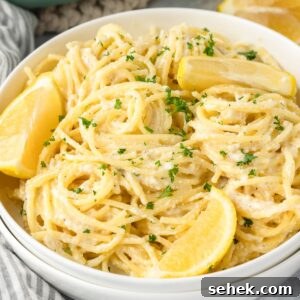 A bowl of creamy pasta garnished with lemon wedges and sprinkled with chopped parsley.