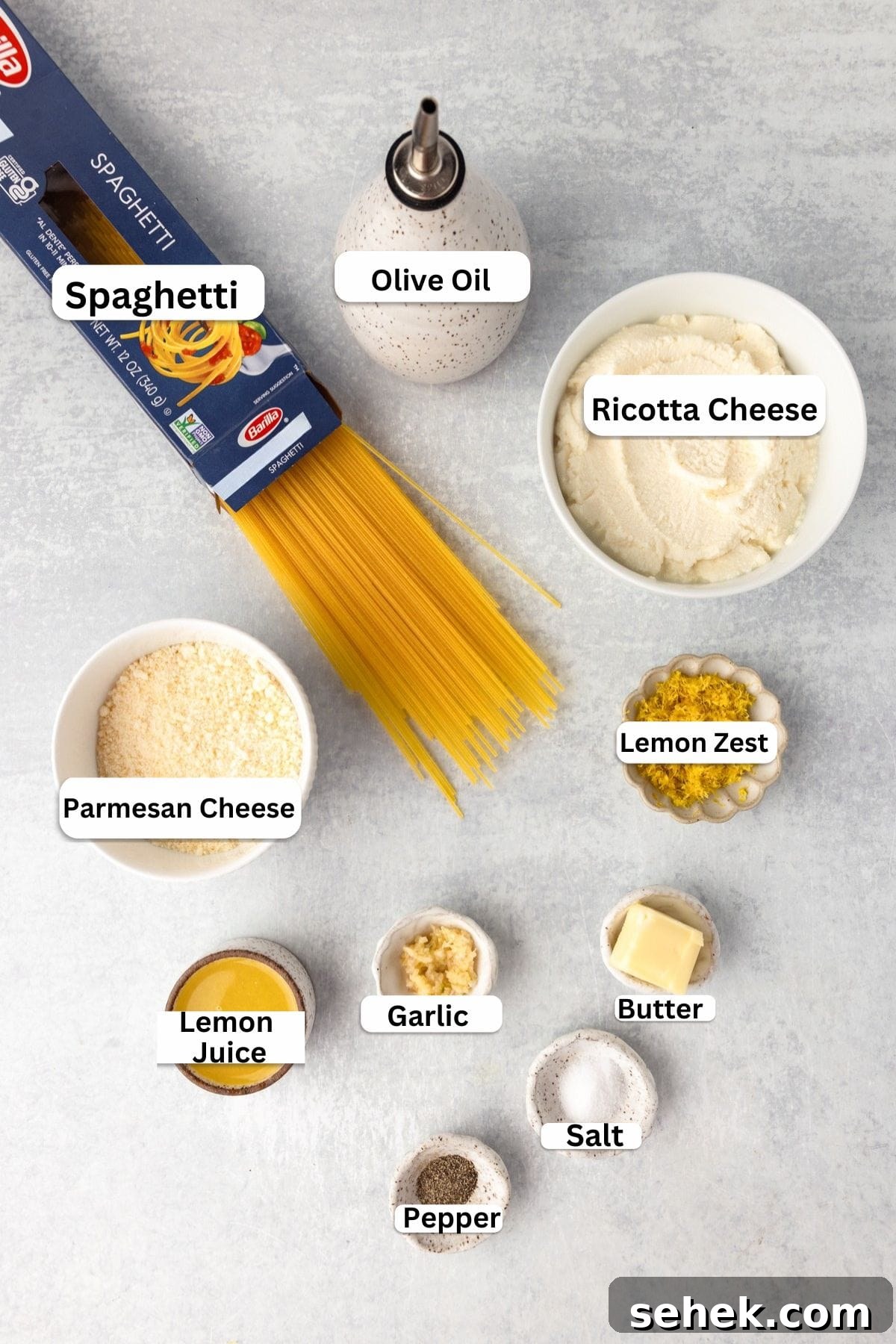 Creamy Lemon Ricotta Pasta with Garlic and Parmesan 3 A top view of ingredients for a pasta dish: spaghetti, olive oil, ricotta cheese, Parmesan cheese, lemon zest, lemon juice, garlic, butter, salt, and pepper.