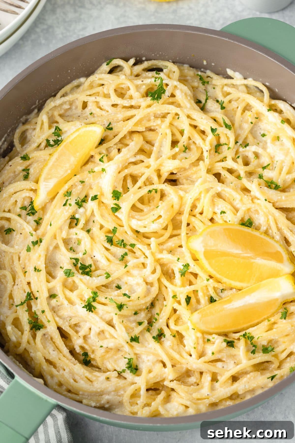 Creamy Lemon Ricotta Pasta with Garlic and Parmesan 5 A close-up of a creamy spaghetti dish in a pot, garnished with chopped parsley and lemon wedges.
